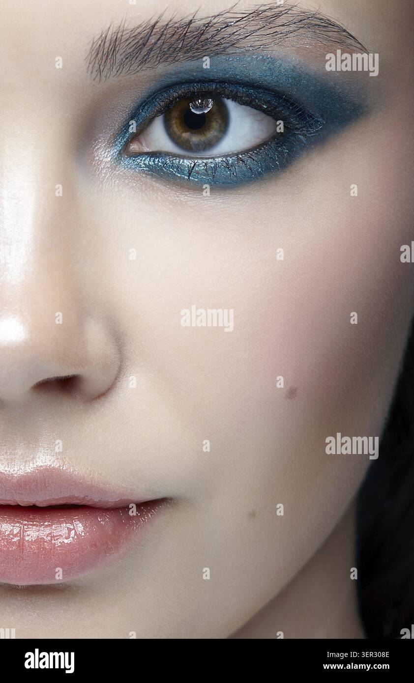 Primo piano macro ritratto del volto femminile. Donna umana mezza faccia con trucco di bellezza serale. Ragazza con pelle perfetta e ombre blu-verdi per gli occhi Foto Stock