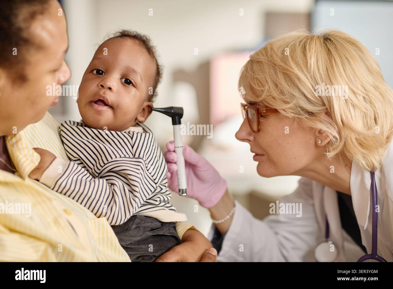 Madre nera che tiene in mano il bambino durante l'esame pediatrico dell'orecchio Foto Stock