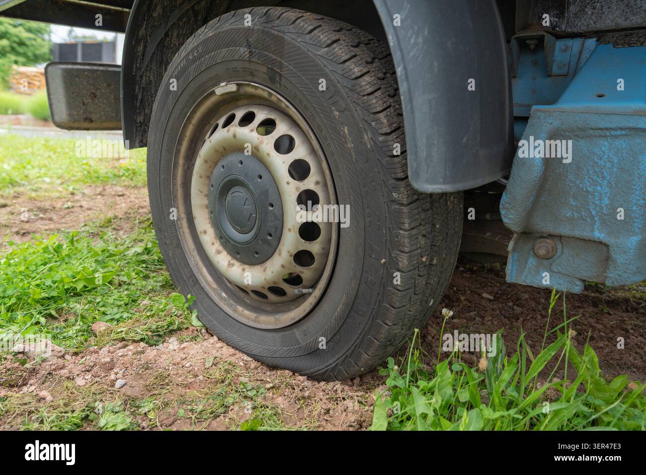 Primo piano di uno pneumatico forato in piano di un autocarro commerciale parcheggiato su terreno sterrato e erba verde in un cantiere edile. Ruota sgonfiata e. Foto Stock