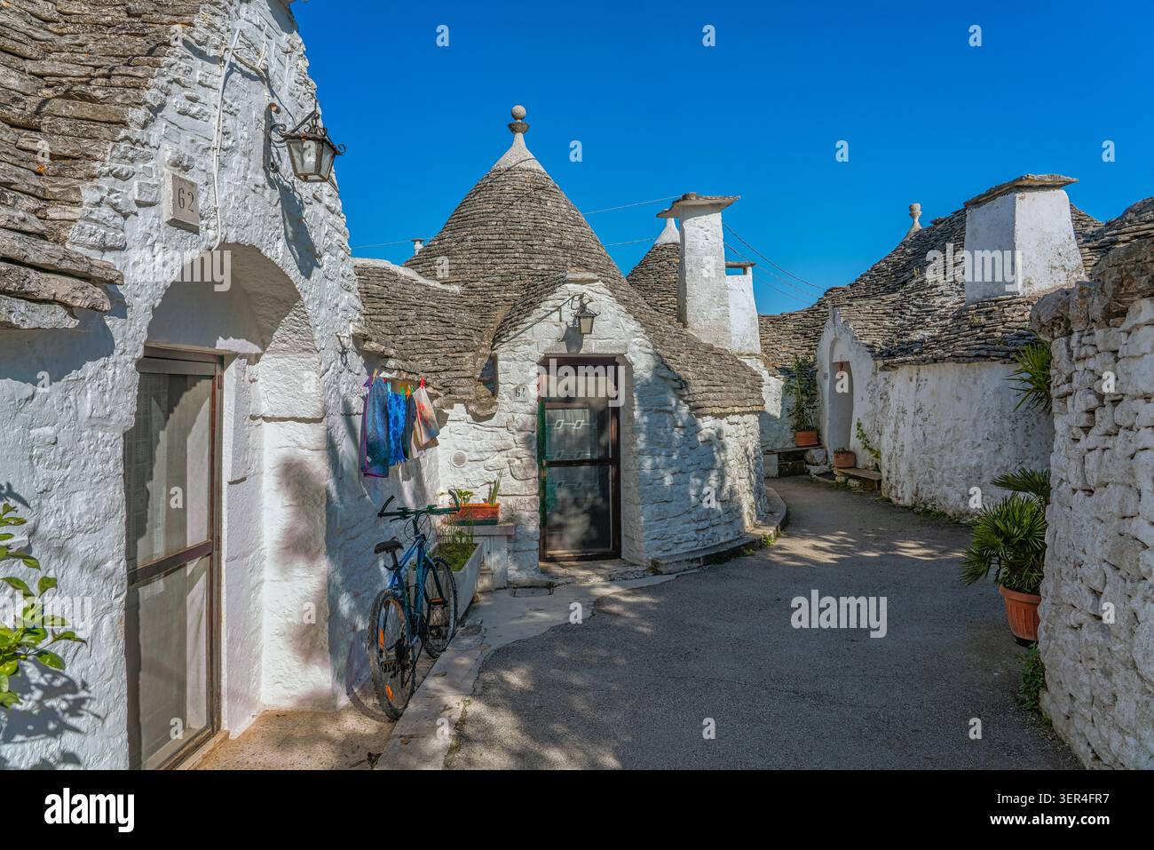 Case a trulli imbiancate con tetti conici in pietra e vasi in terracotta lungo un vicolo tranquillo, Rione Monti, Alberobello, provincia di Bari, Puglia, Italia Foto Stock