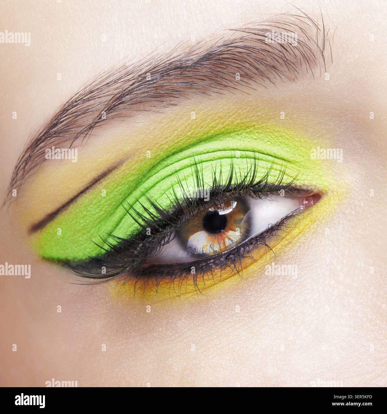 Primo piano macro di occhio umano femminile. Donna con un trucco di bellezza per il viso di moda. Ragazza con ombre verdi e gialle agli occhi Foto Stock