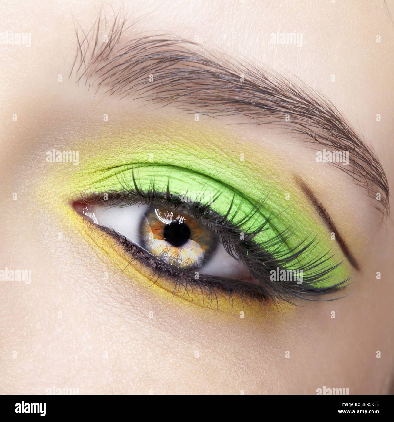 Primo piano macro di occhio umano femminile. Donna con un trucco di bellezza per il viso di moda. Ragazza con ombre verdi e gialle agli occhi Foto Stock