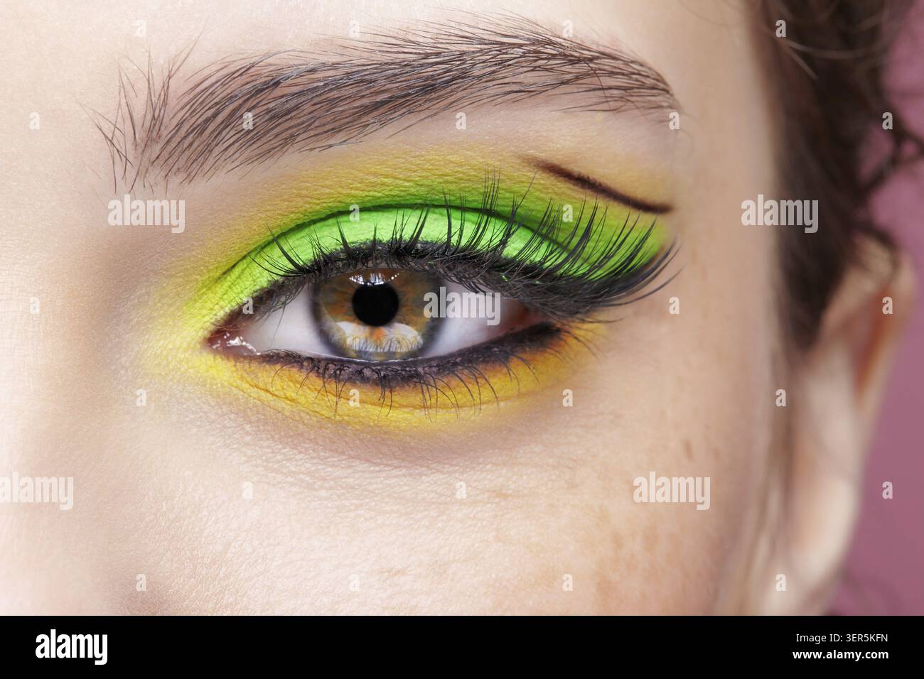 Primo piano macro di occhio umano femminile. Donna con un trucco di bellezza per il viso di moda. Ragazza con ombre verdi e gialle agli occhi Foto Stock