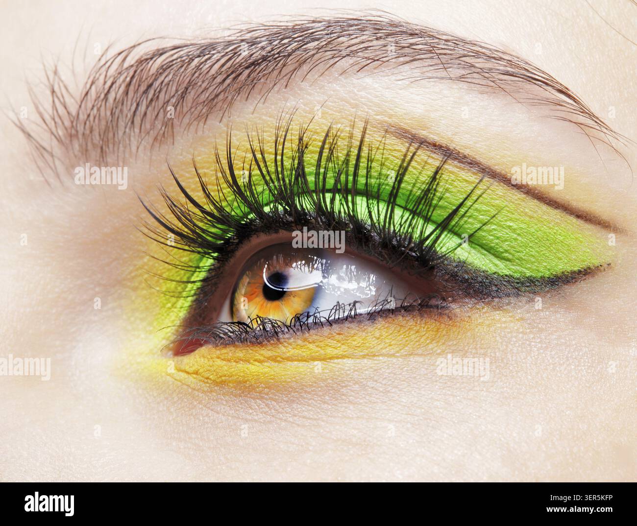 Primo piano macro di occhio umano femminile. Donna con un trucco di bellezza per il viso di moda. Ragazza con ombre verdi e gialle agli occhi Foto Stock