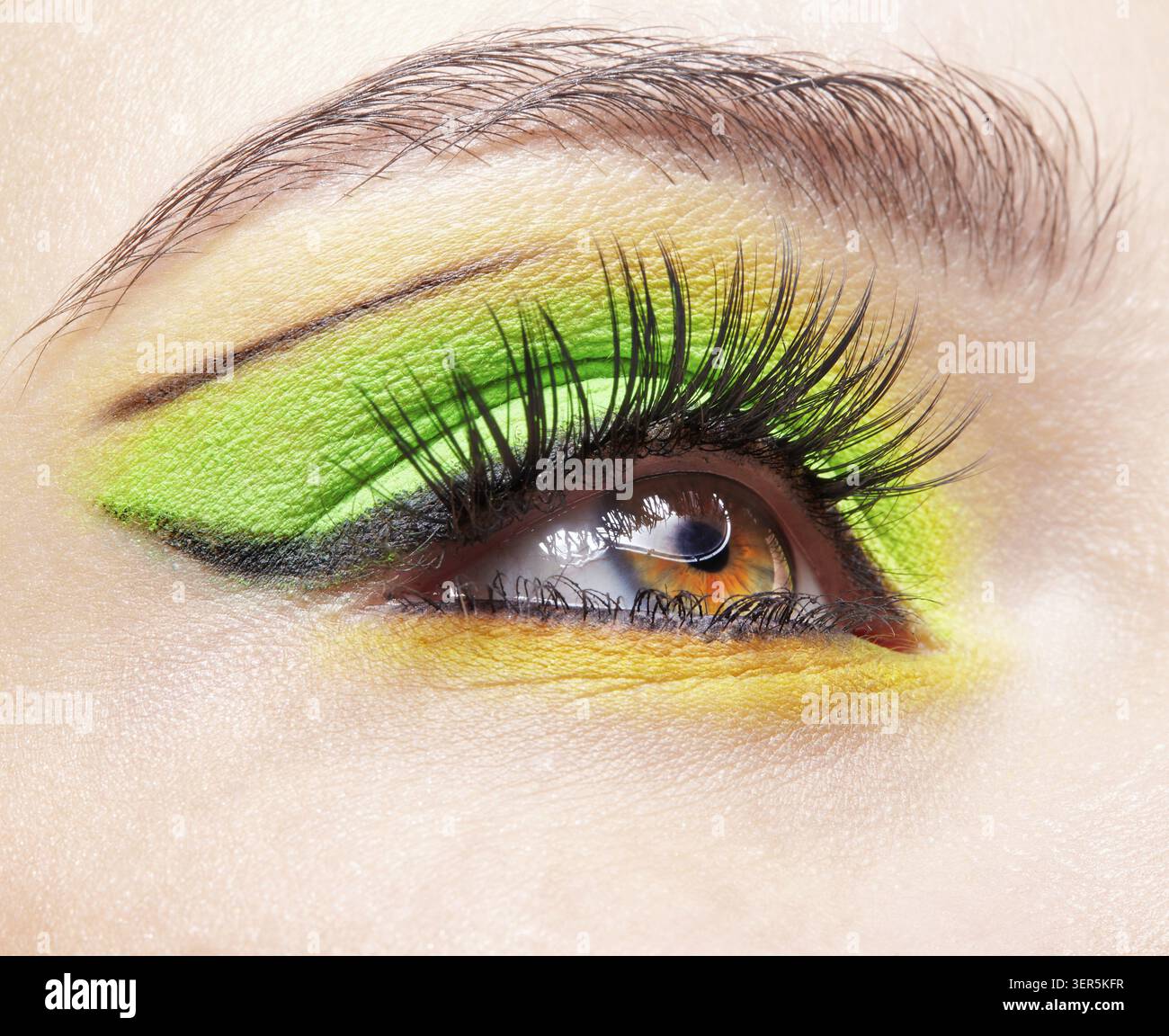 Primo piano macro di occhio umano femminile. Donna con un trucco di bellezza per il viso di moda. Ragazza con ombre verdi e gialle agli occhi Foto Stock