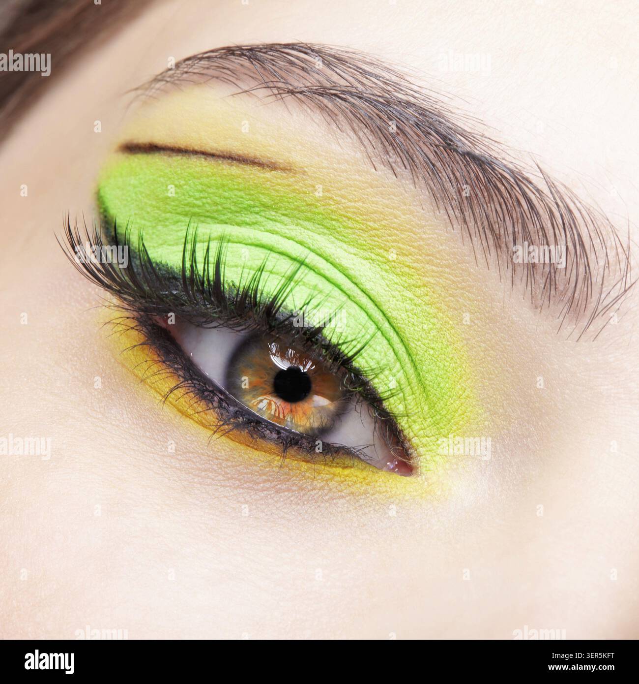 Primo piano macro di occhio umano femminile. Donna con un trucco di bellezza per il viso di moda. Ragazza con ombre verdi e gialle agli occhi Foto Stock