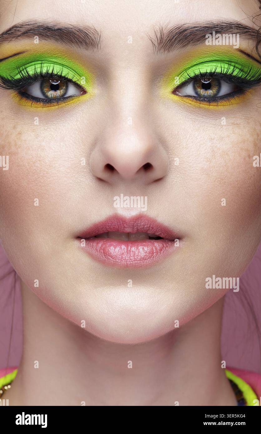 Ritratto di una giovane donna su sfondo rosa. Donna con insoliti occhi verdi ombre trucco, capelli ricci e orecchini Foto Stock