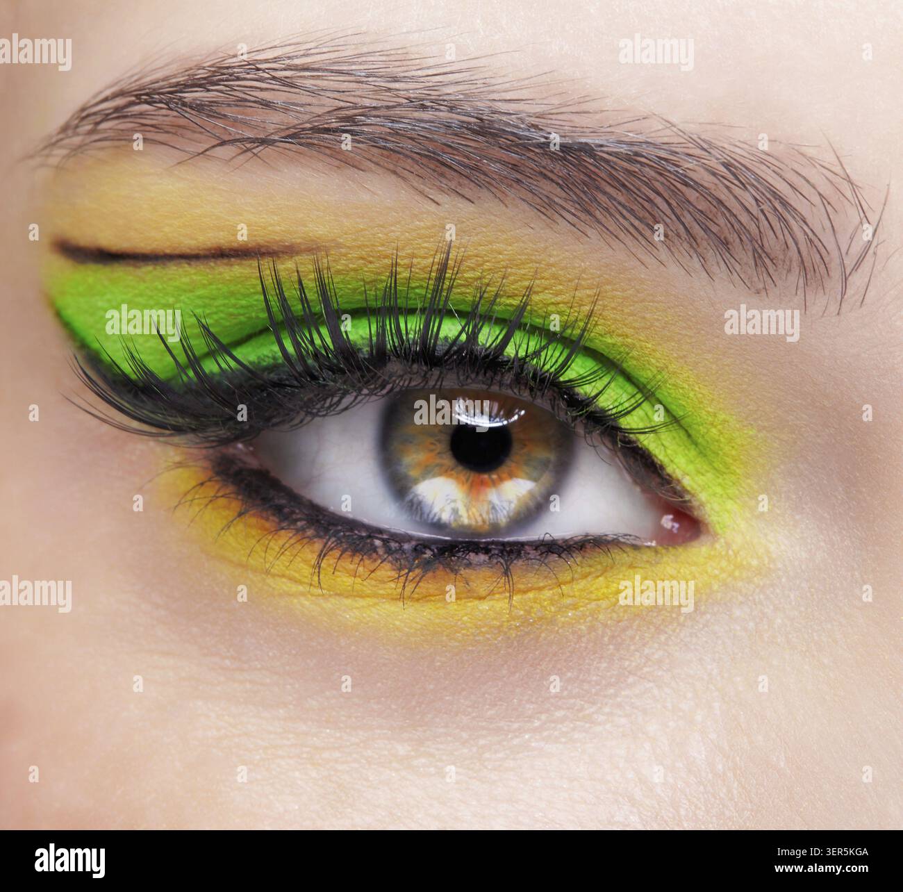 Primo piano macro di occhio umano femminile. Donna con un trucco di bellezza per il viso di moda. Ragazza con ombre verdi e gialle agli occhi Foto Stock