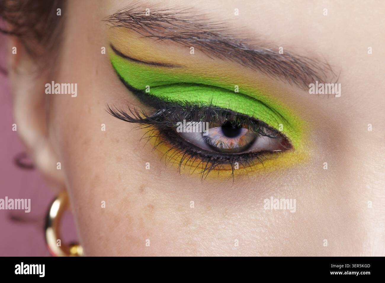 Primo piano macro di occhio umano femminile. Donna con un trucco di bellezza per il viso di moda. Ragazza con ombre verdi e gialle agli occhi Foto Stock