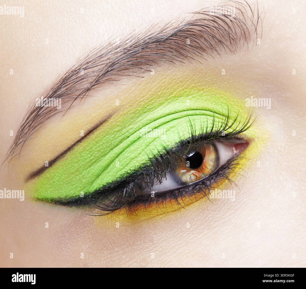 Primo piano macro di occhio umano femminile. Donna con un trucco di bellezza per il viso di moda. Ragazza con ombre verdi e gialle agli occhi Foto Stock