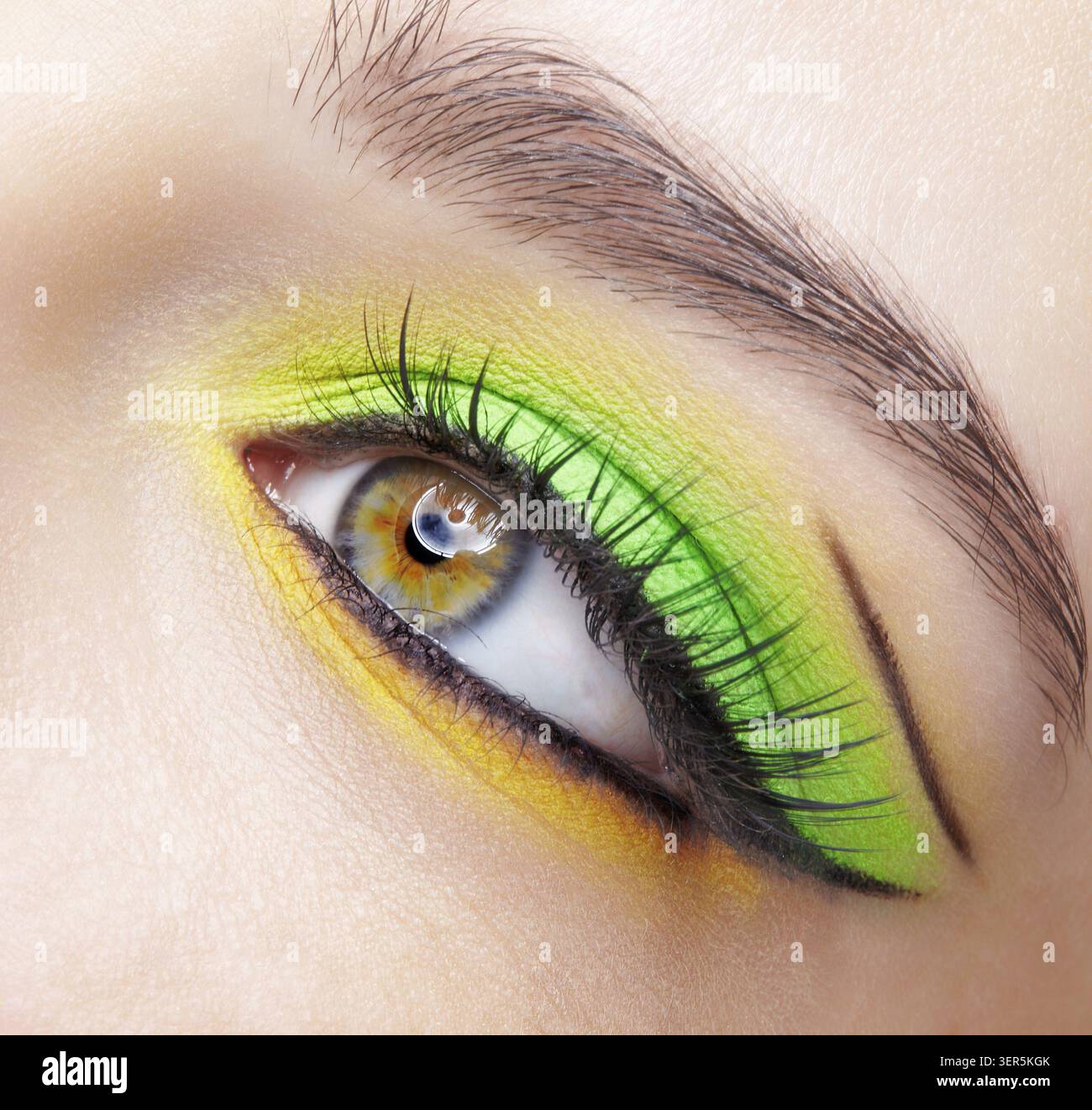 Primo piano macro di occhio umano femminile. Donna con un trucco di bellezza per il viso di moda. Ragazza con ombre verdi e gialle agli occhi Foto Stock