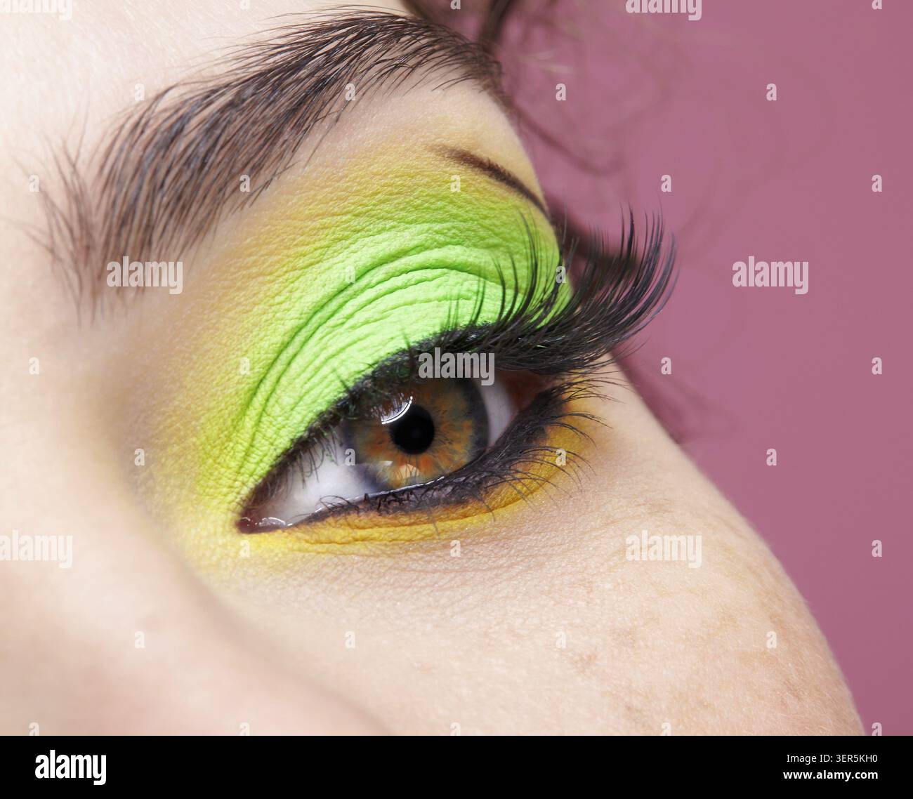 Primo piano macro di occhio umano femminile. Donna con un trucco di bellezza per il viso di moda. Ragazza con ombre verdi e gialle agli occhi Foto Stock