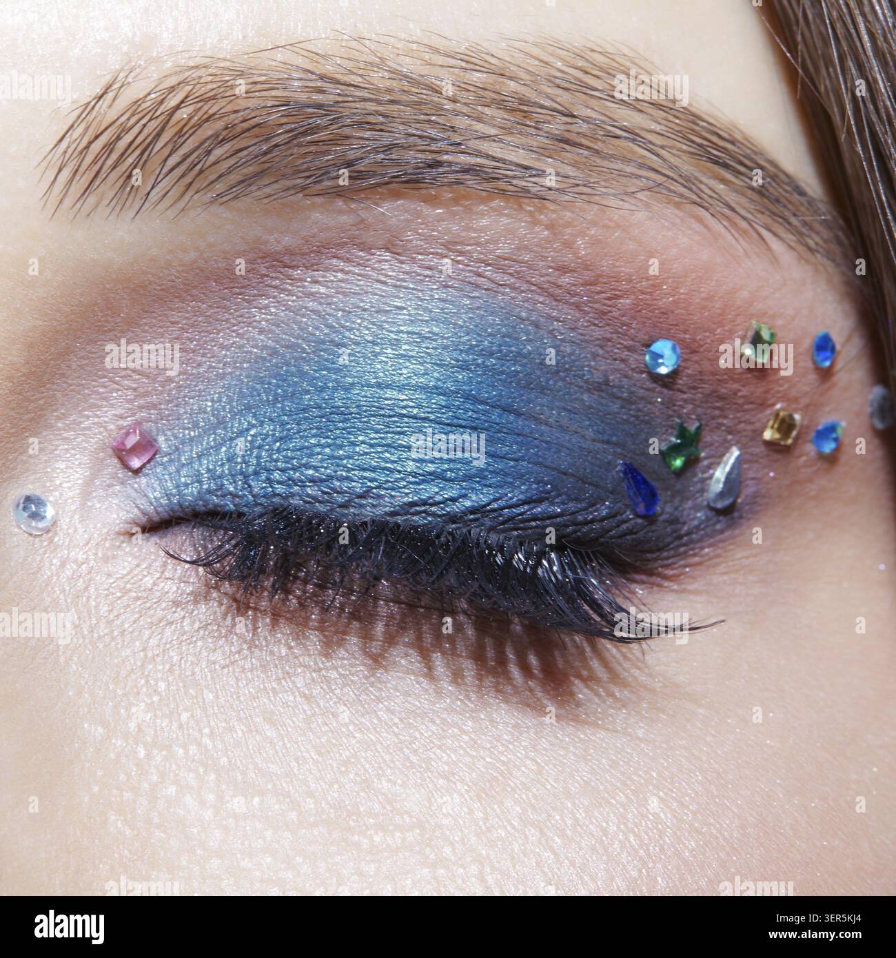 Foto macro di primo piano di un occhio umano femminile chiuso con ombre blu e strass. Donna con trucco naturale per la sera Foto Stock