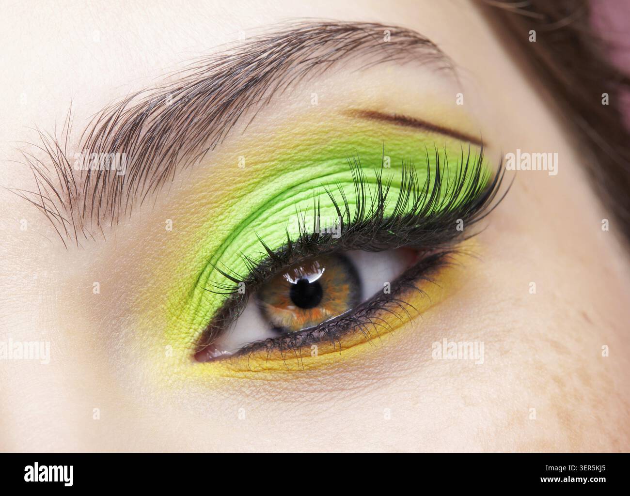 Primo piano macro di occhio umano femminile. Donna con un trucco di bellezza per il viso di moda. Ragazza con ombre verdi e gialle agli occhi Foto Stock