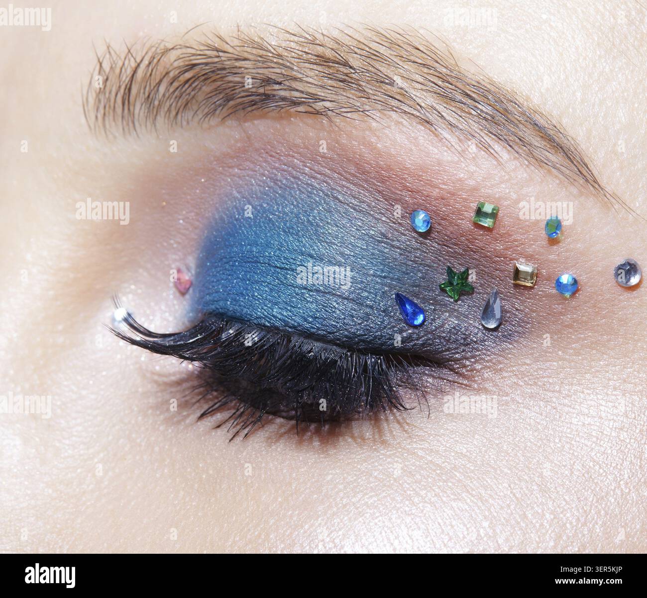 Foto macro di primo piano di un occhio umano femminile chiuso con ombre blu e strass. Donna con trucco naturale per la sera Foto Stock