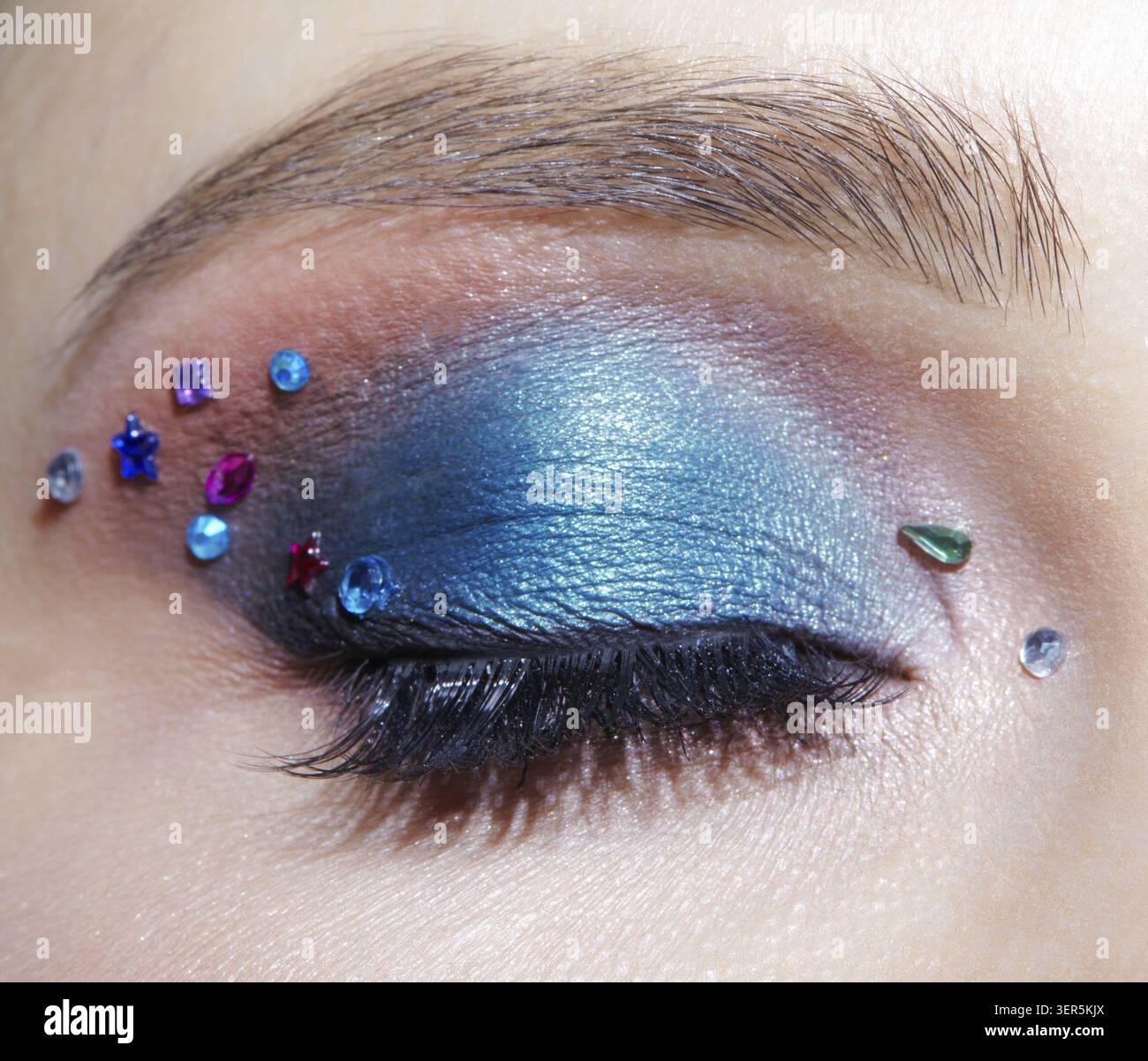Foto macro di primo piano di un occhio umano femminile chiuso con ombre blu e strass. Donna con trucco naturale per la sera Foto Stock