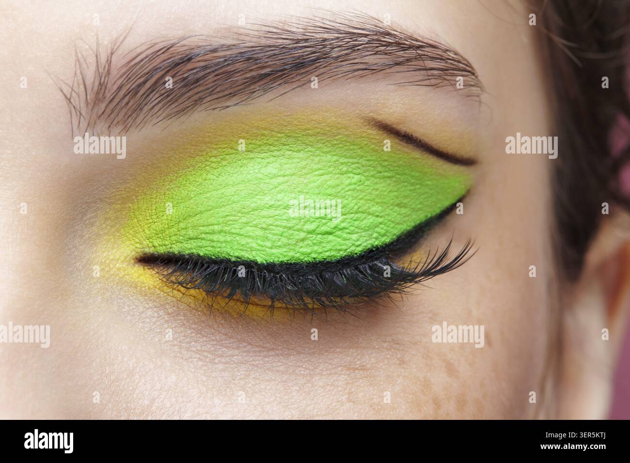 Foto macro di primo piano di un occhio umano femminile chiuso. Donna con un trucco di bellezza per il viso di moda. Ragazza con pelle perfetta e ombre verdi e gialle agli occhi Foto Stock