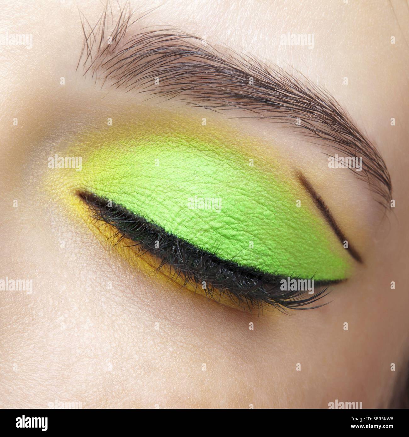 Foto macro di primo piano di un occhio umano femminile chiuso. Donna con un trucco di bellezza per il viso di moda. Ragazza con pelle perfetta e ombre verdi e gialle agli occhi Foto Stock