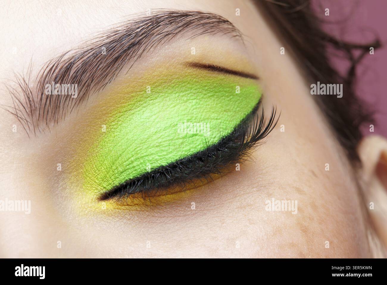 Foto macro di primo piano di un occhio umano femminile chiuso. Donna con un trucco di bellezza per il viso di moda. Ragazza con pelle perfetta e ombre verdi e gialle agli occhi Foto Stock