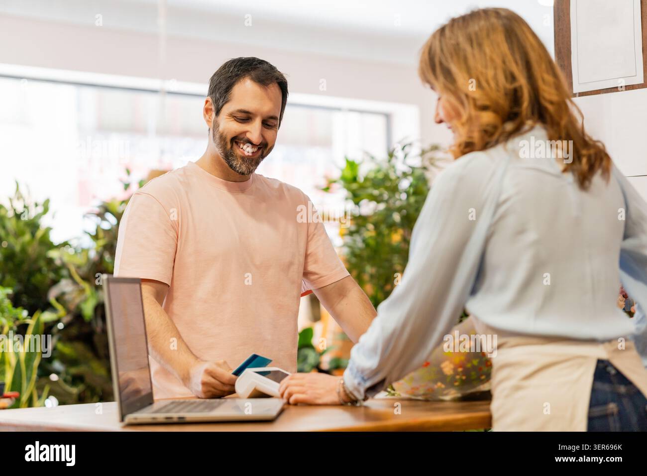 Fiorista sorridente che tiene in mano il lettore di carte di credito mentre un cliente donna paga con lo smartphone utilizzando la tecnologia nfc Foto Stock