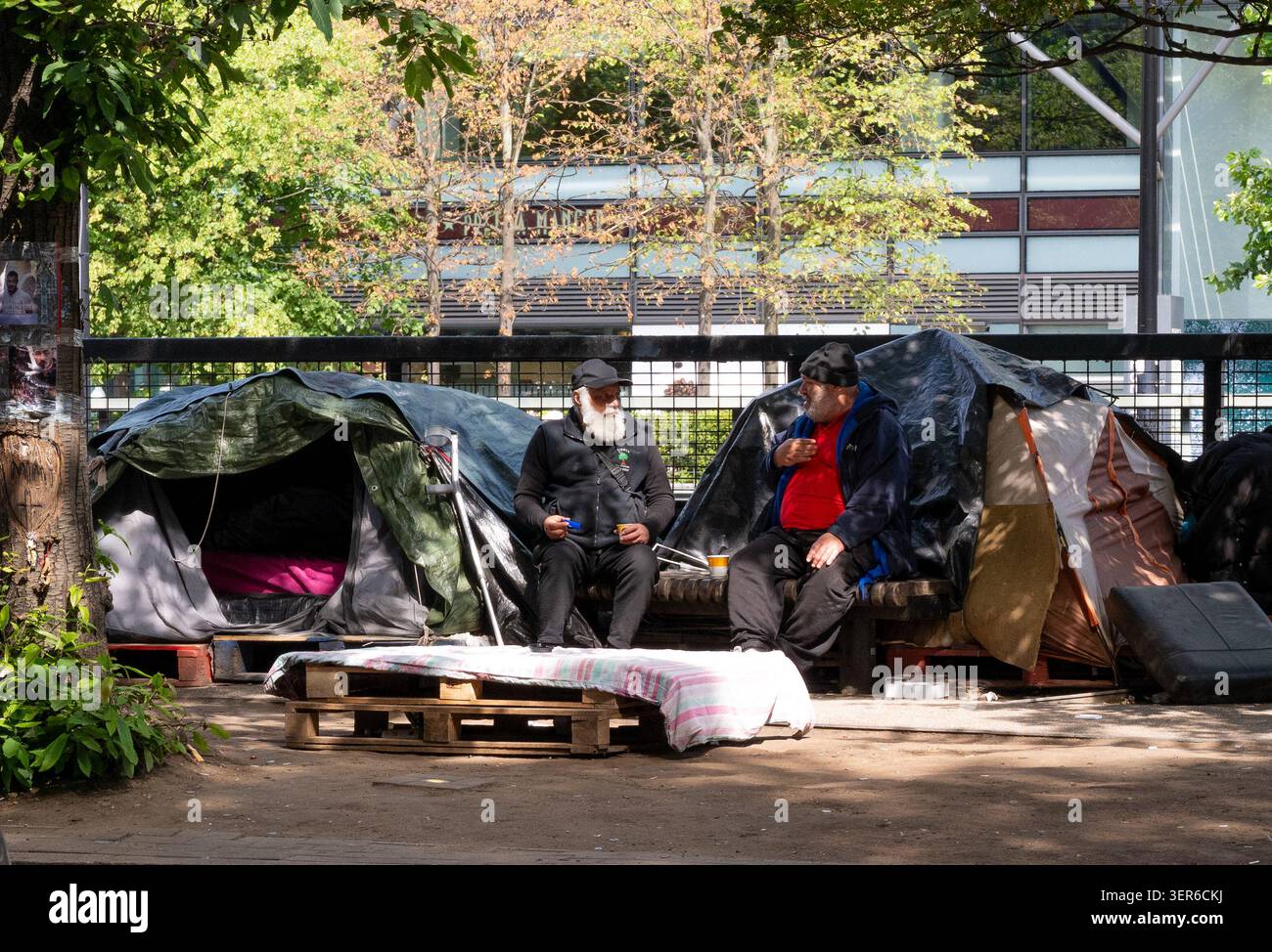 Due anziani si siedono a parlare, a fumare e a bere caffè fuori dalle tende in un accampamento di Euston Road, nel centro di Londra, Regno Unito Foto Stock