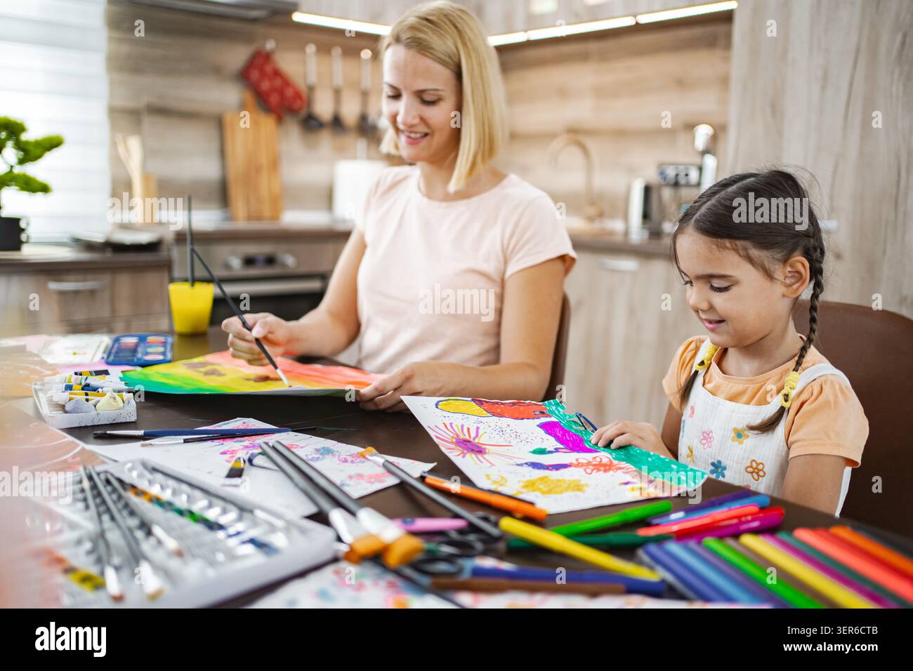 Madre e figlia si divertono con una sessione d'arte creativa a casa, mostrando insieme i loro disegni colorati Foto Stock