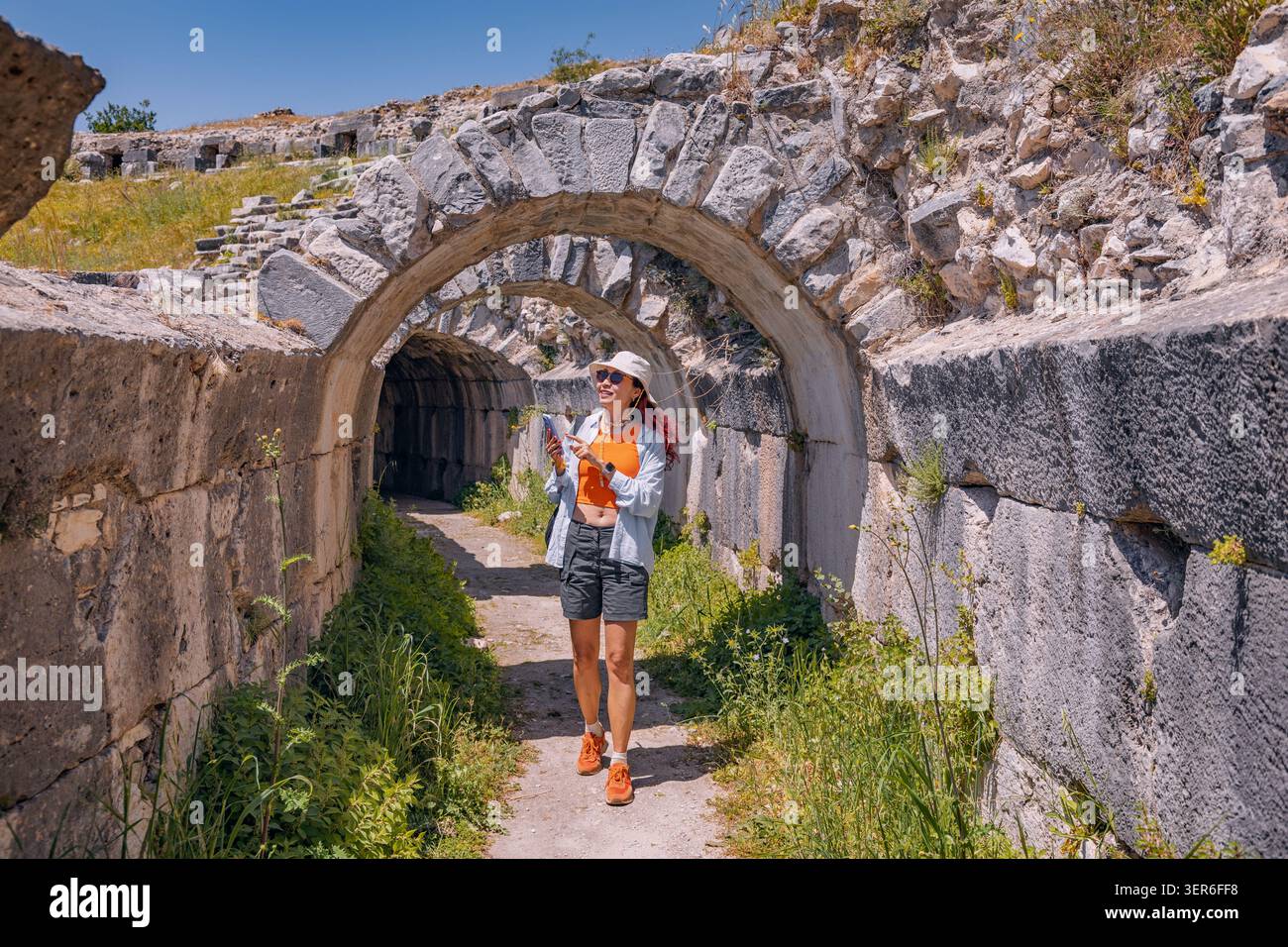 Donna turistica che cammina attraverso l'arco in pietra nel sito storico della città di Mileto, sperimentando viaggi, storia, civiltà antica Foto Stock