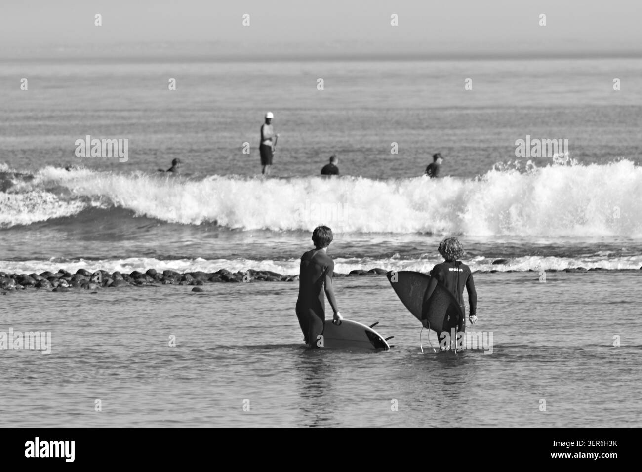 Gruppo principiante che tiene lezioni di surf tenendo tavole in acque poco profonde di Malibu preparandosi a remare verso onde infranti. Foto Stock