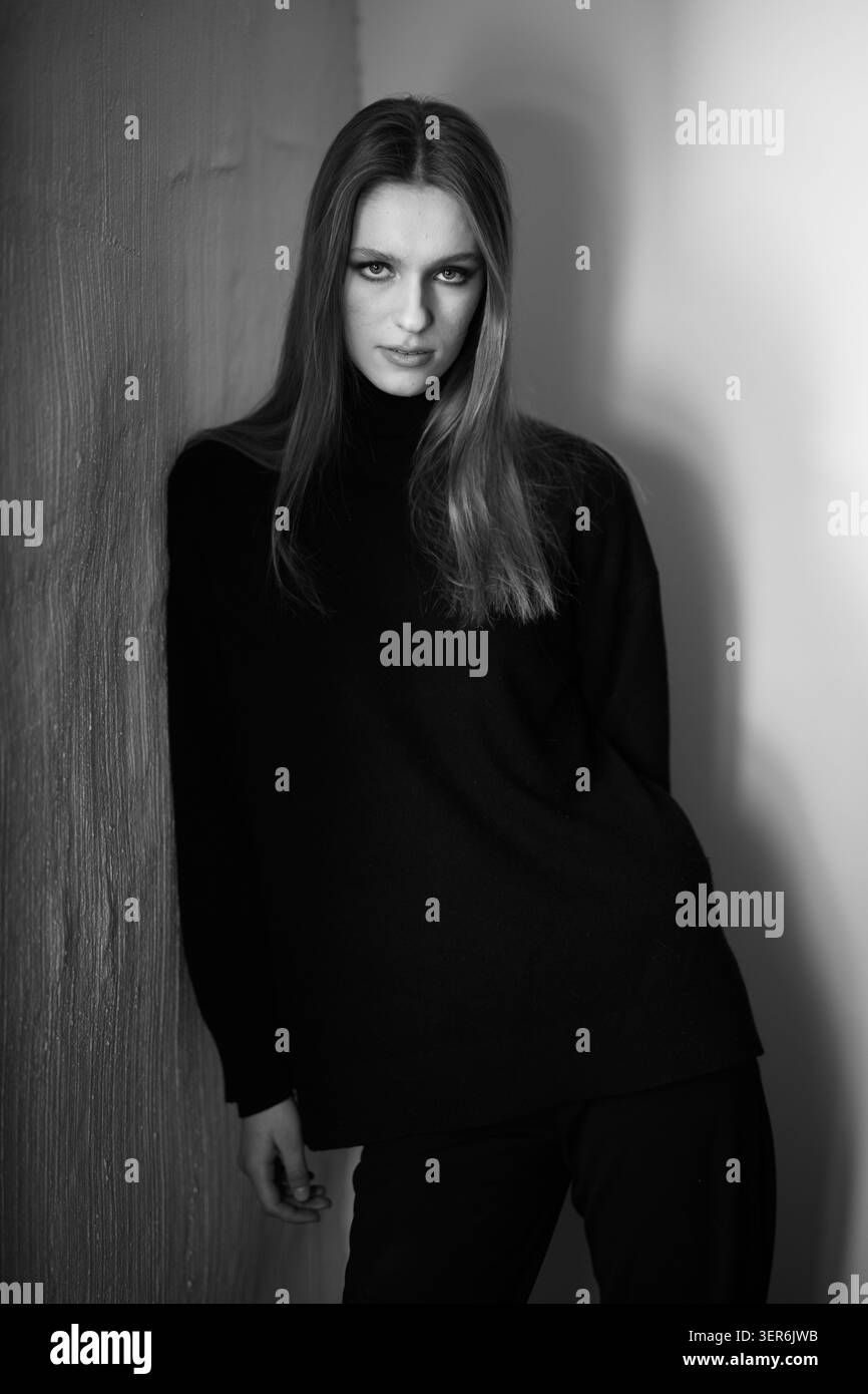 Drammatico ritratto in bianco e nero di una donna appoggiata contro un muro. Il contrasto profondo, l'illuminazione strutturata e lo sguardo forte creano un sofisticato AN Foto Stock