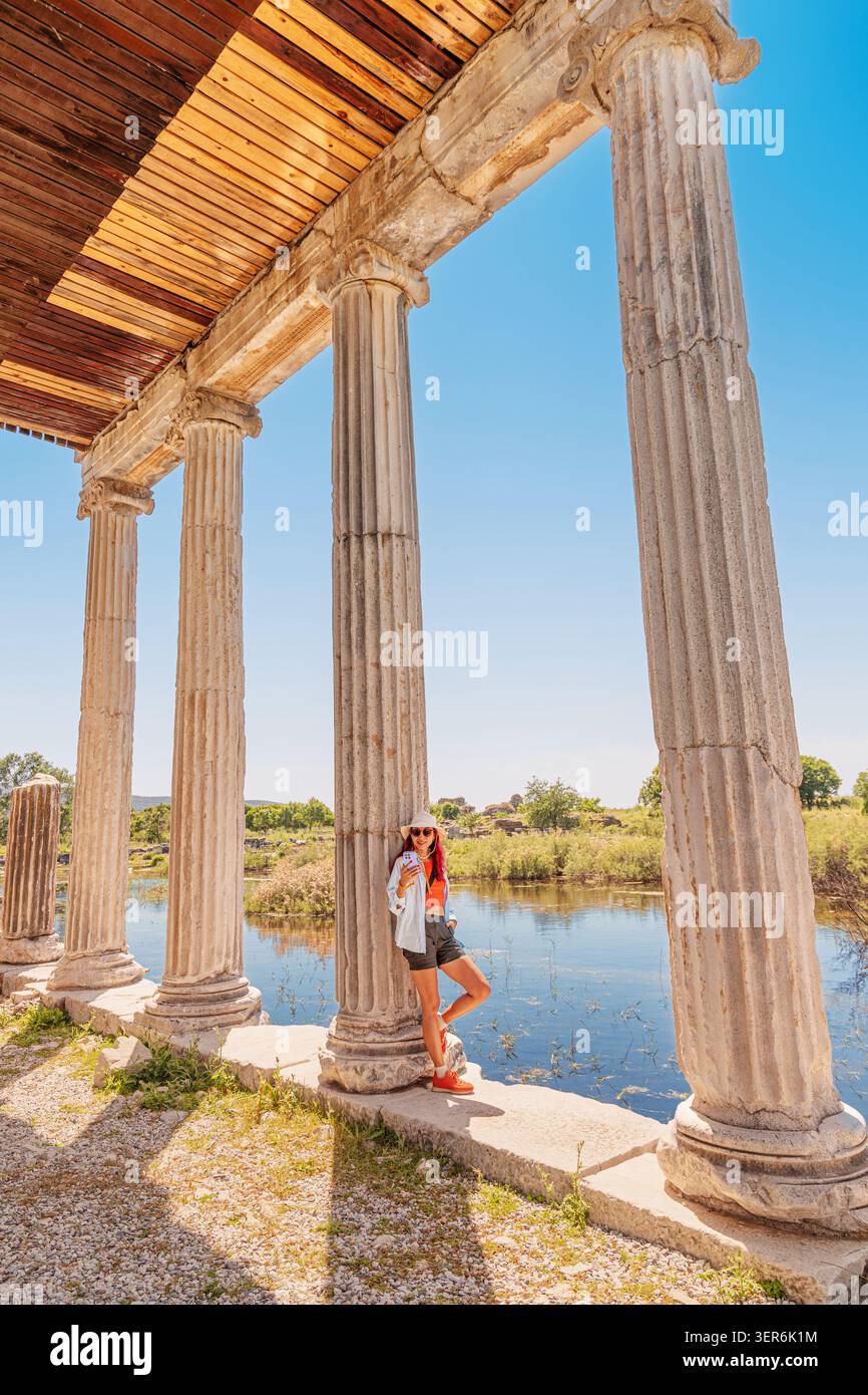 Donna in piedi accanto alle antiche colonne del Tempio di Mileto, Turkiye, che riflette sulla storia e sui viaggi Foto Stock