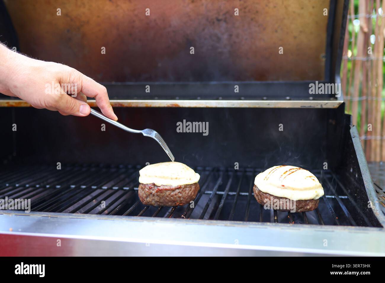 Primo piano di cheeseburger cucinati su un barbecue caldo, perfetto per feste sul cortile e riunioni di famiglia. Foto Stock