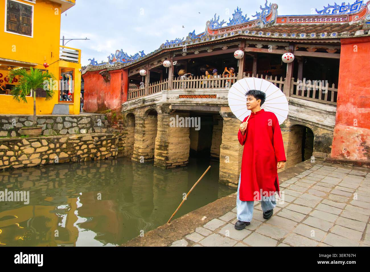 Giovane con abiti tradizionali di fronte allo storico ponte coperto giapponese a Hol An Vietnam. Il ponte fu costruito alla fine del XVI secolo da Ja Foto Stock