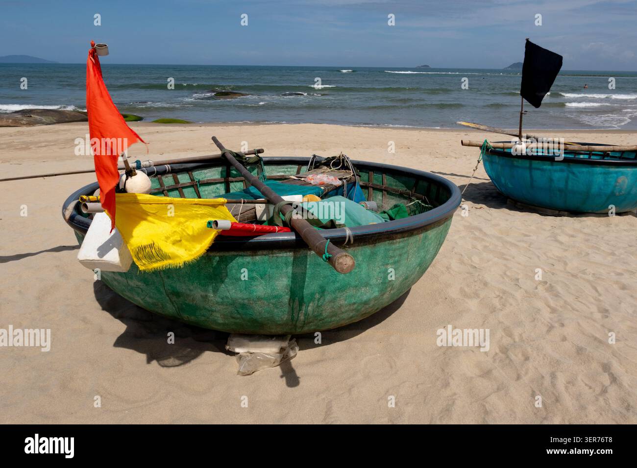 Piccola barca da pesca verde circolare con bandiere colorate, reti e attrezzature da pesca. Sulla spiaggia di Cua dai vicino a Hoi An Vietnam Foto Stock