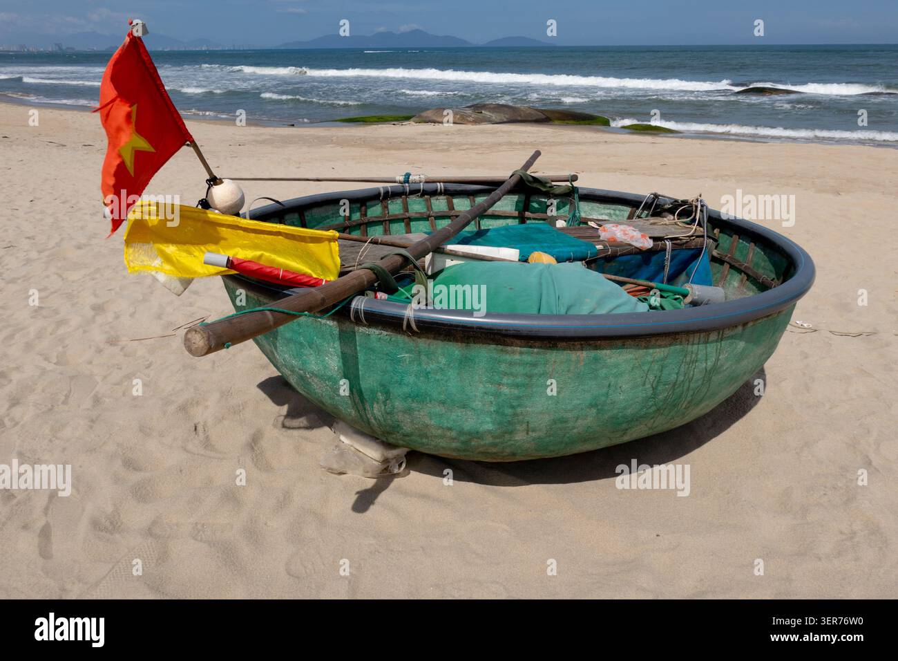 Piccola barca da pesca verde circolare con bandiere colorate, reti e attrezzi da pesca sulla spiaggia di Cua Dai vicino a Hoi An, Vietnam Foto Stock
