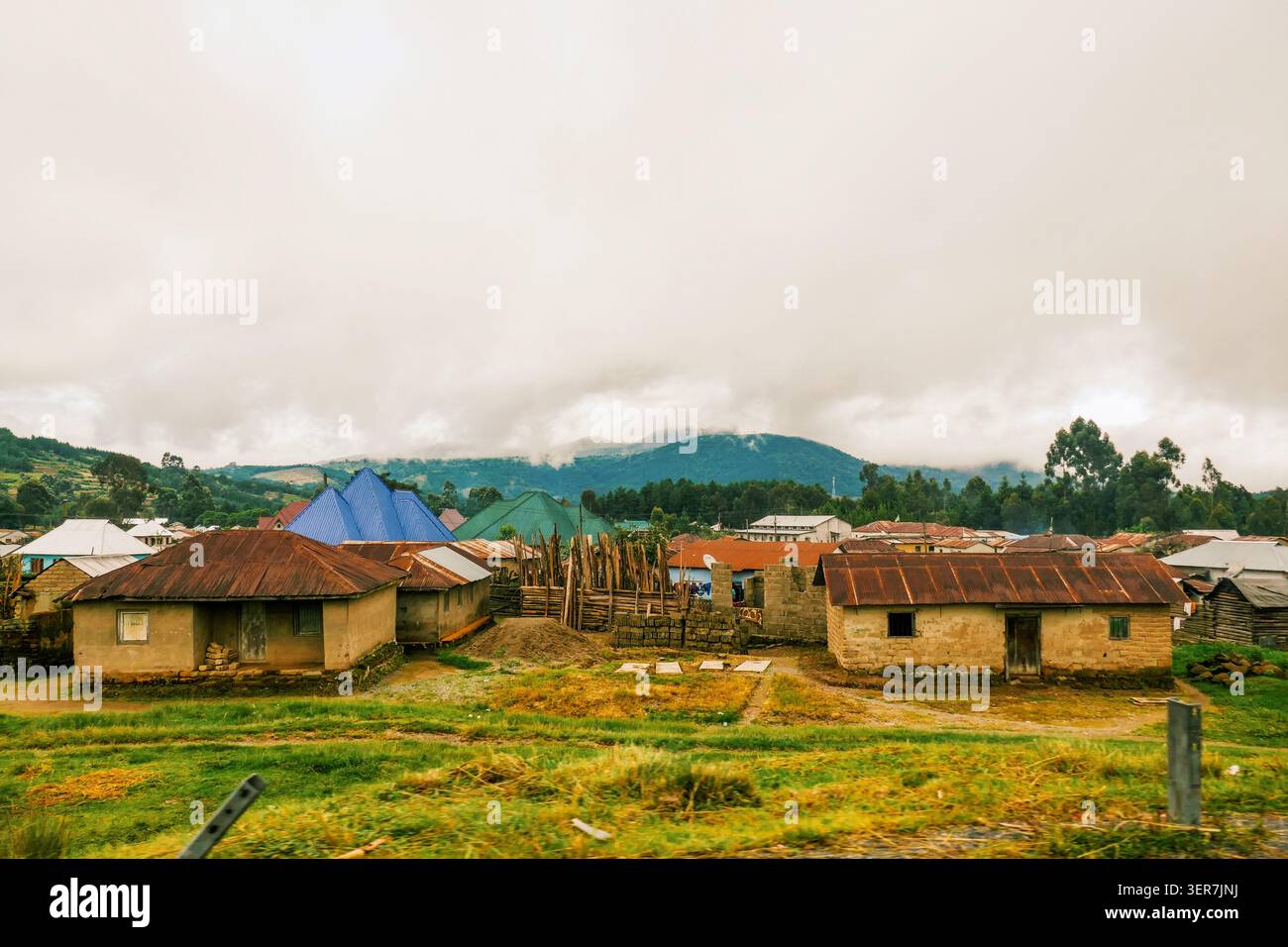 Paesaggio rurale panoramico di Mbeya Town, Tanzania, con case e lussureggianti colline verdi sotto un cielo nuvoloso Foto Stock