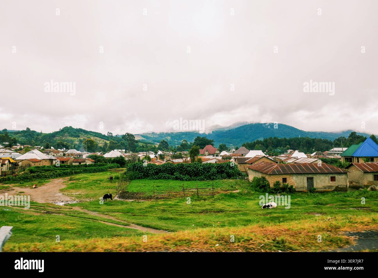 Paesaggio rurale panoramico di Mbeya Town, Tanzania, con case e lussureggianti colline verdi sotto un cielo nuvoloso Foto Stock