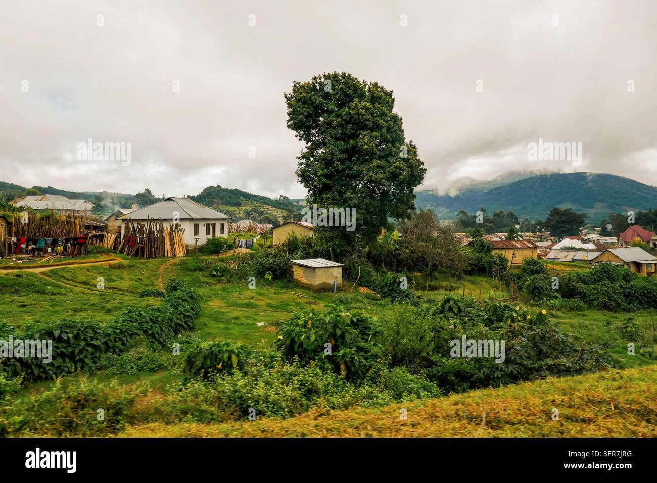 Paesaggio rurale panoramico di Mbeya Town, Tanzania, con case e lussureggianti colline verdi sotto un cielo nuvoloso Foto Stock