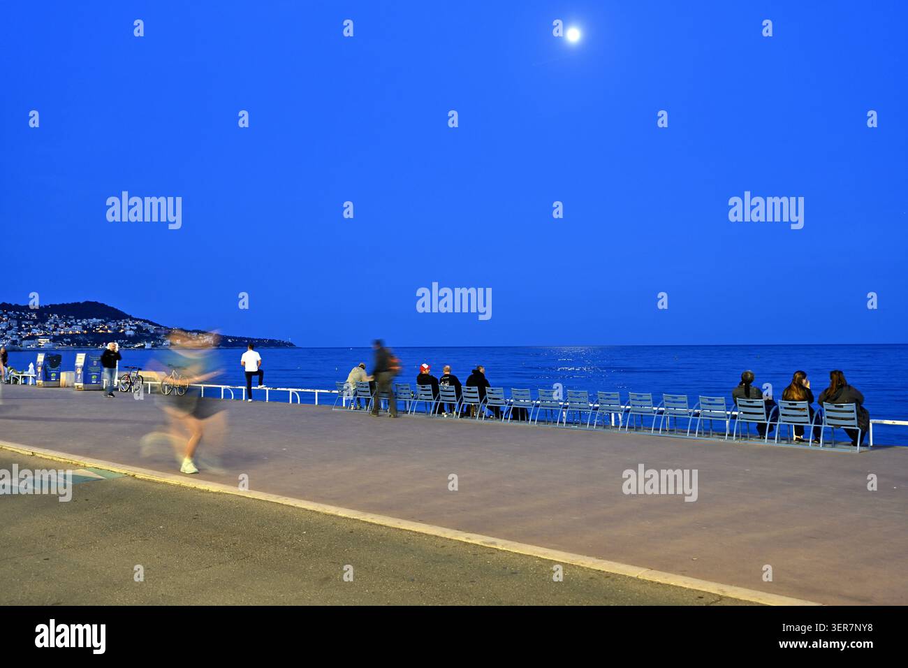 Persone che camminano, corrono, si siedono lungo la Promenade des Anglais in prima serata e si affacciano sul Mar Mediterraneo, Nizza, Francia Foto Stock