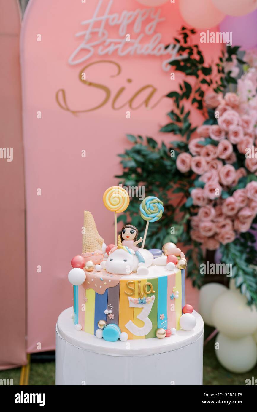 Torta di compleanno colorata con unicorno con palloncini e fiori Foto Stock