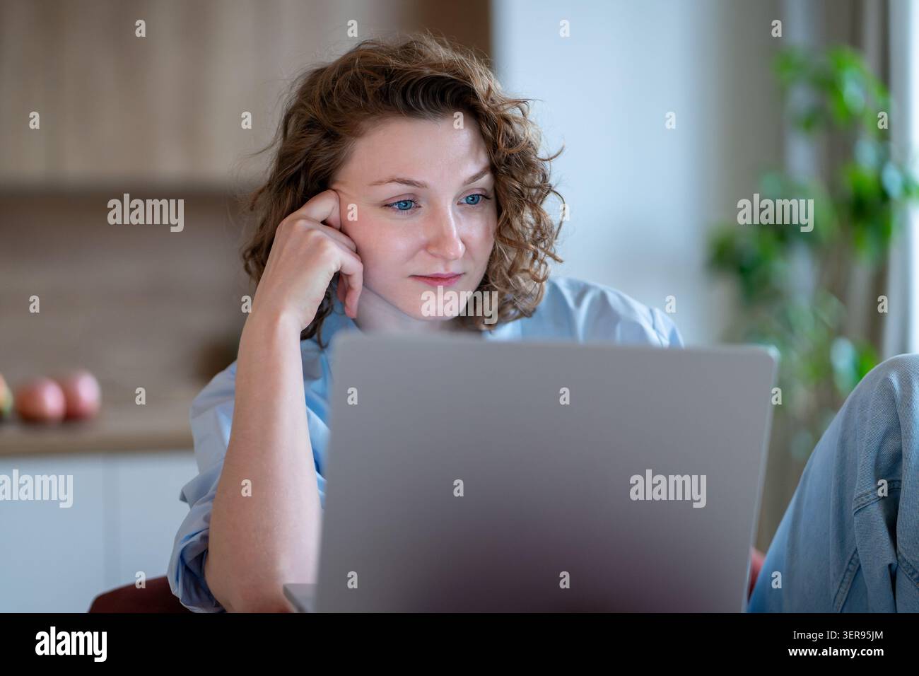 Donna concentrata e premurosa, seduta comodamente a casa, che lavora da remoto utilizzando un computer portatile, che studia online. Foto Stock
