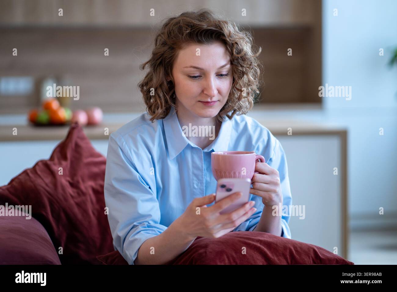 Donna interessata che guarda lo schermo telefono leggere notizie, navigare sul Web mentre fa una pausa caffè a casa. Foto Stock