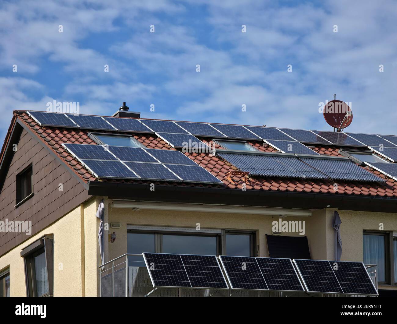 vecchia casa tradizionale con pannelli solari sul tetto e moduli solari per balconi che mostrano una transizione di energia rinnovabile a prezzi accessibili Foto Stock