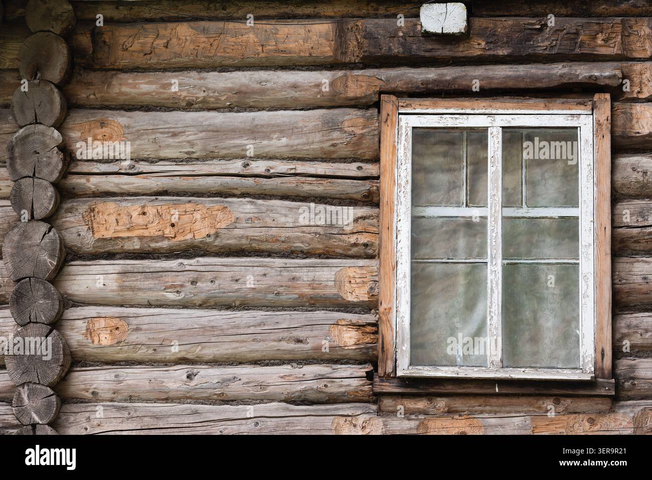 Una parete in legno con capanna in legno intemperie caratterizzata da una finestra sbucciata con cornici bianche e pannelli di vetro. Rustica, texture vintage e venatura in legno naturale conferiscono alta qualità Foto Stock
