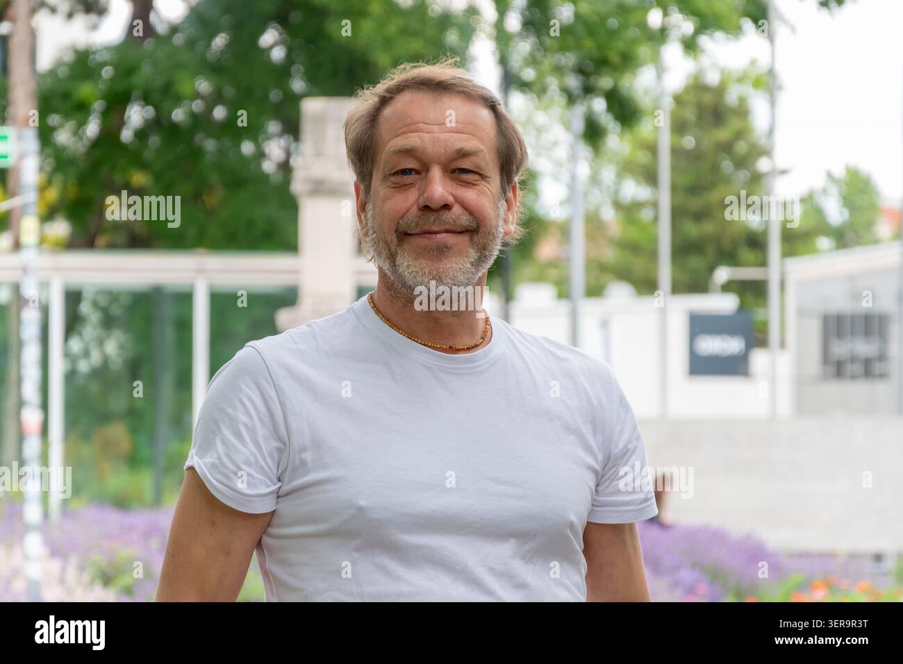 Uomo di circa 55 anni in piedi contro l'architettura urbana e il verde Foto Stock