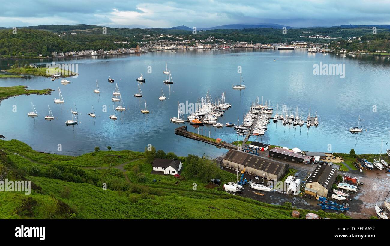 Una tranquilla vista aerea sulla baia di Oban, dove le barche a vela riposano sulle acque calme sotto i cieli spettacolari della costa occidentale della Scozia Foto Stock