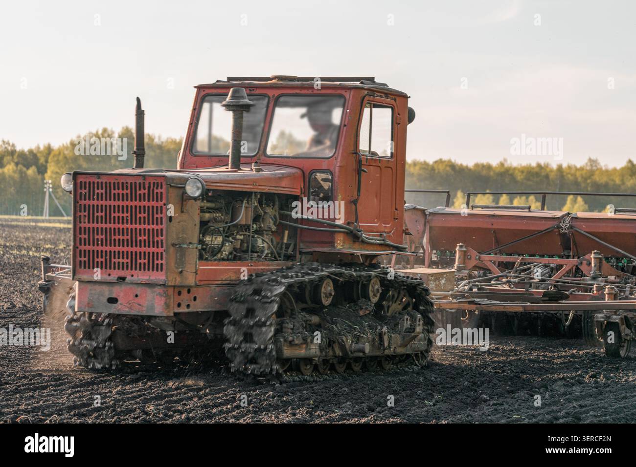 Trattore cingolato che opera su terreni agricoli coltivati durante il traino di una seminatrice durante la stagione di semina. Macchine agricole in azione, lavoro sul campo, prodotto pr Foto Stock