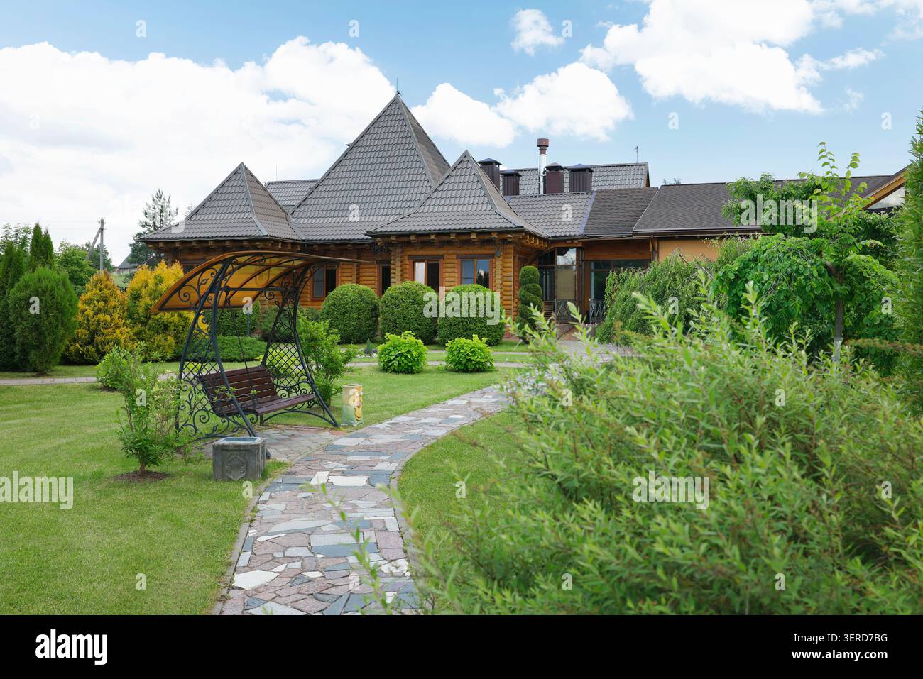 Bellissima villa in legno con vialetto in pietra e accogliente giardino sul prato verde. Lussuosa architettura rustica di cottage in legno circondata da Foto Stock