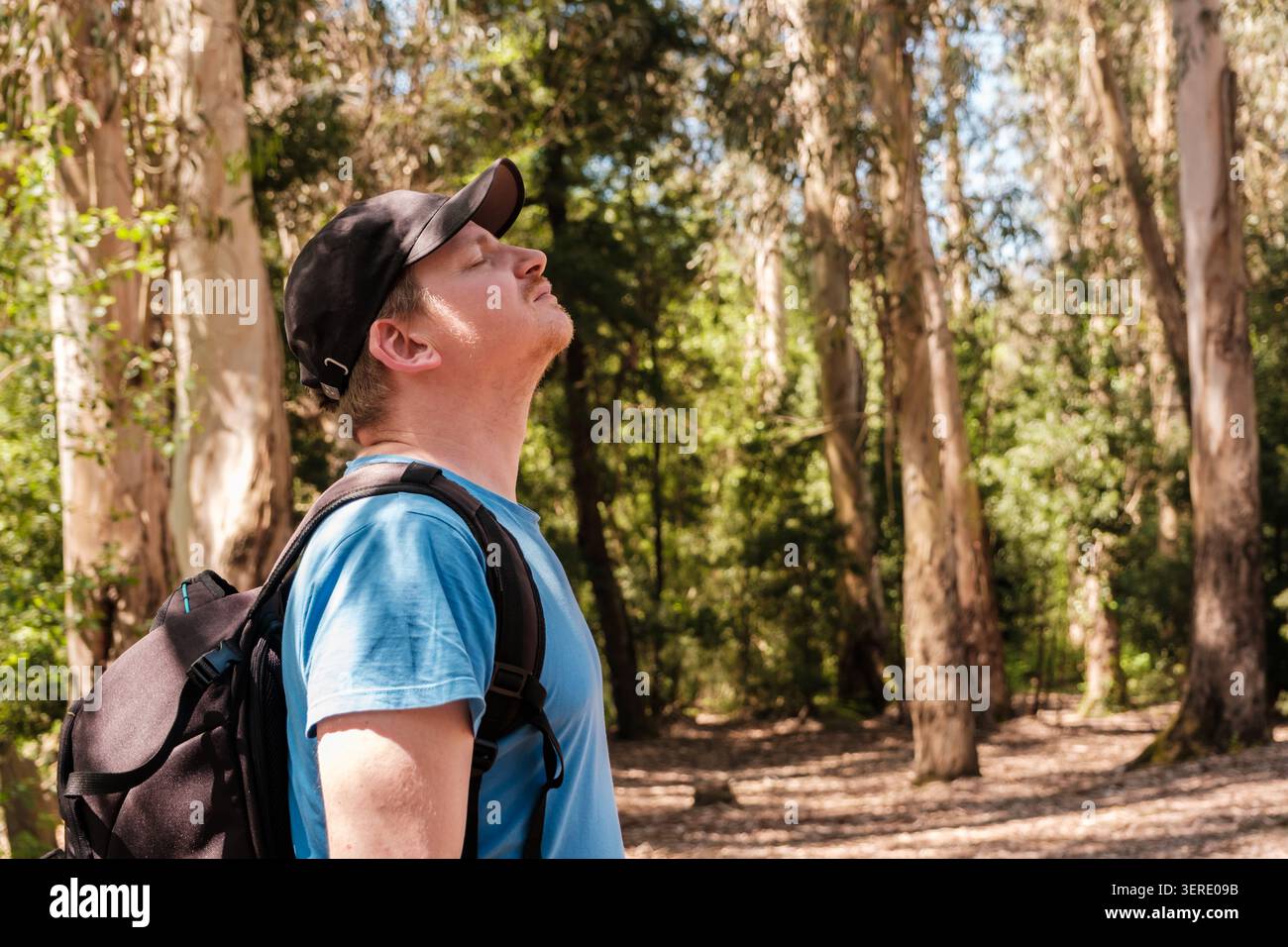 Uomo a occhi chiusi che fa un respiro profondo in una foresta illuminata dal sole e si sente rinfrescato Foto Stock