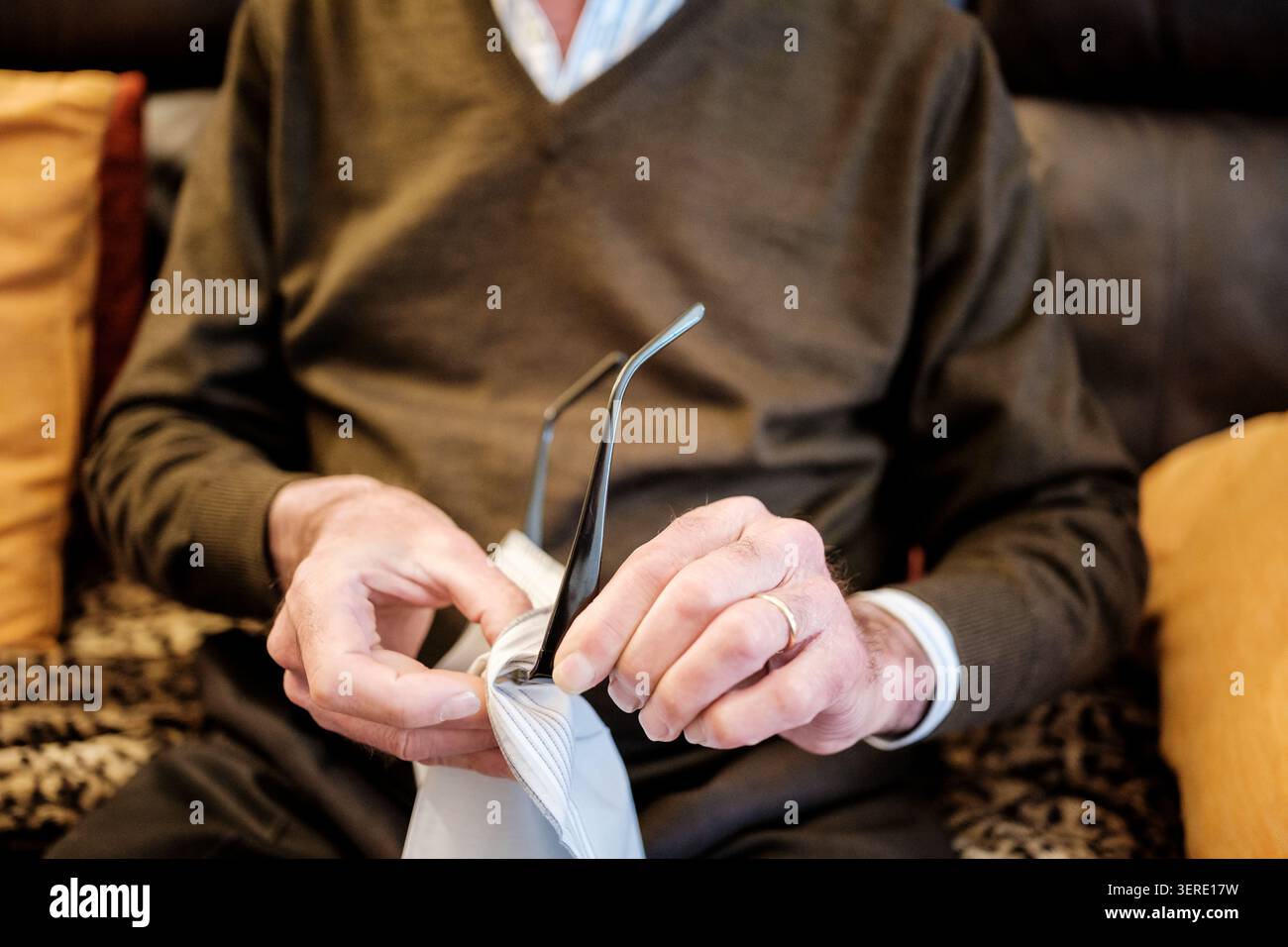 Le mani di un uomo anziano puliscono accuratamente gli occhiali, concentrandosi sulla buona visione e sulla routine quotidiana Foto Stock