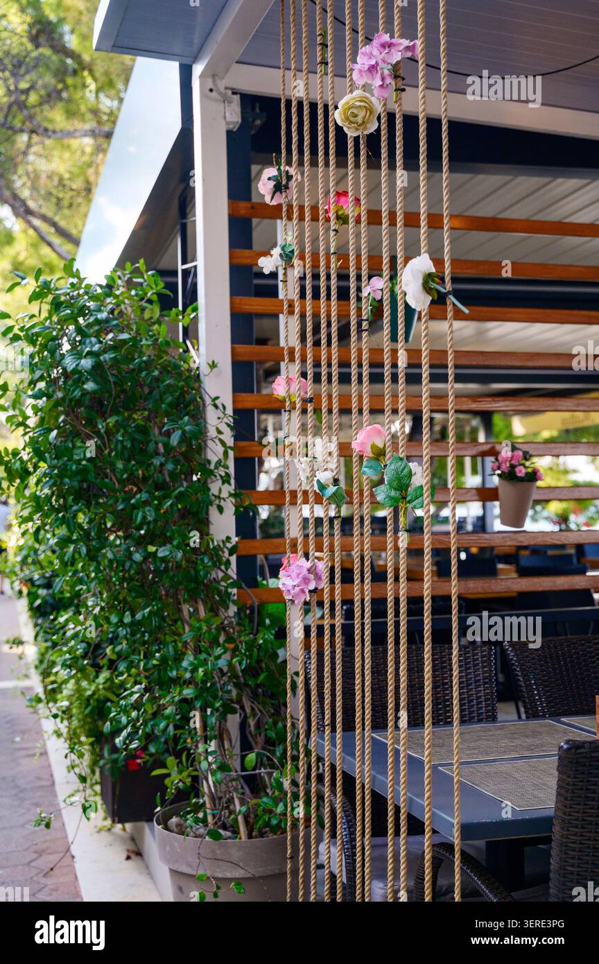 Elegante divisorio verticale in corda decorato con rose artificiali in un elegante caffè all'aperto. Foto Stock